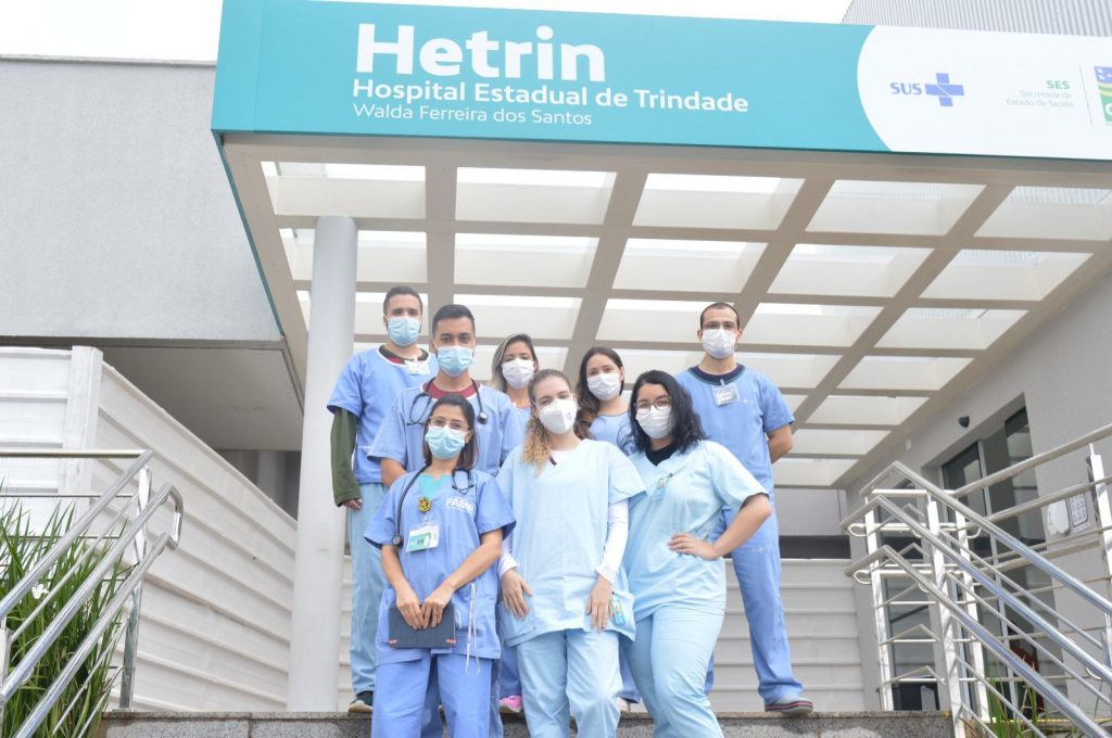 Alunos de medicina, entre meninas e meninos estão a frente do hospital Hetrin nas escadas com roupas no tom azul claro, todos participam do Programa de Estágio Hetrin